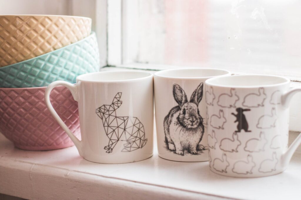 three assorted design ceramic mugs next to a pile of ceramic bowls